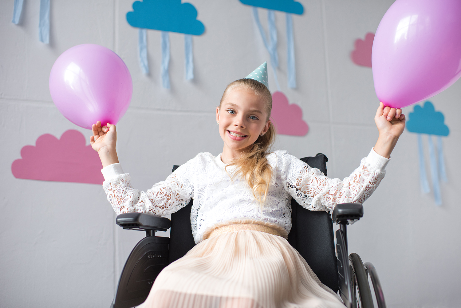 Handicappet pige der sidder i kørestol og har lyserøde balloner i hånden