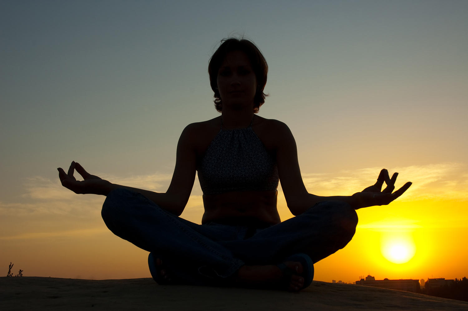 Dame der sidder og meditere ved solnedgang