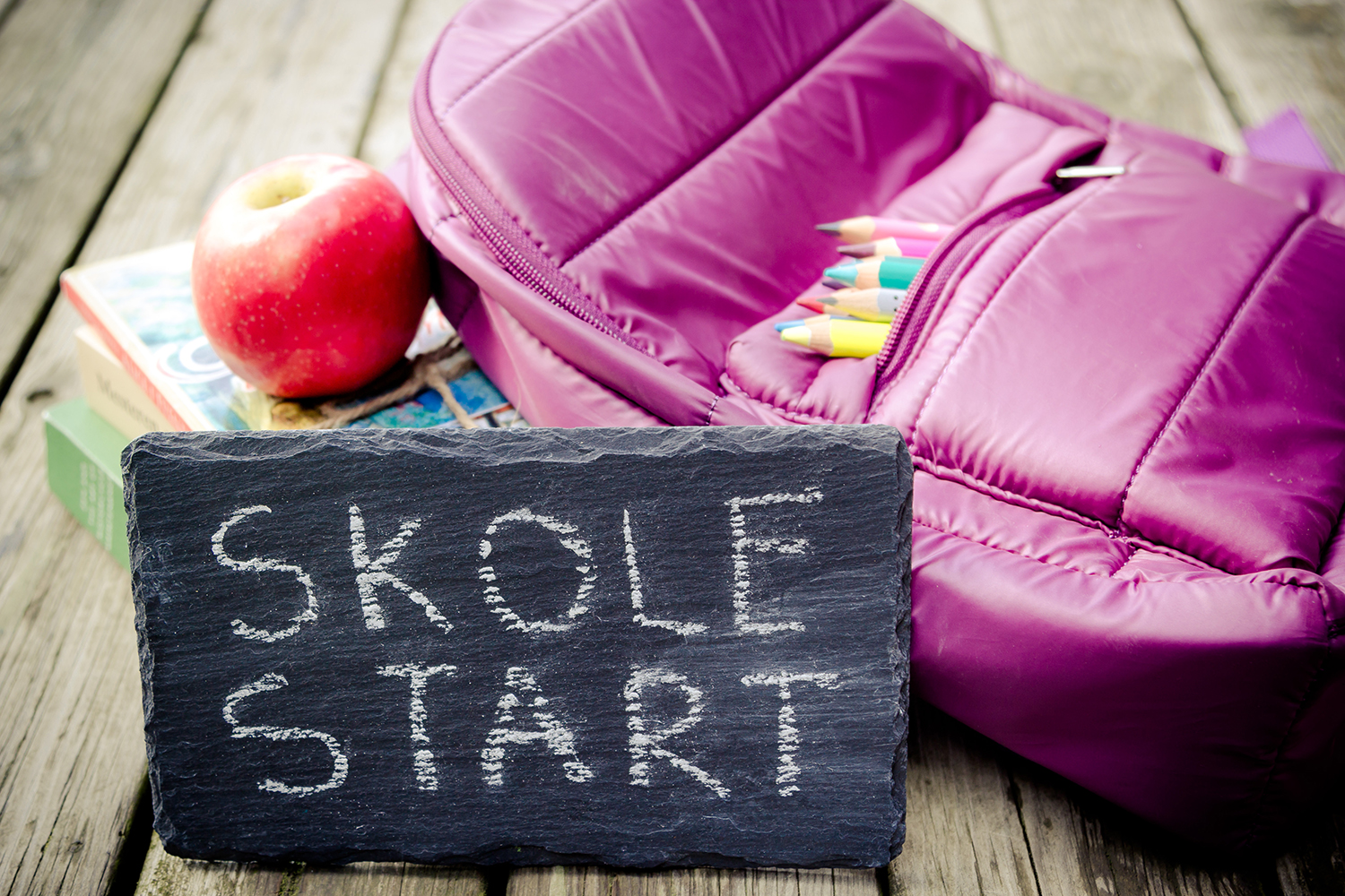 Skilt med skolestart og lilla skoletaske med farveblyanter i